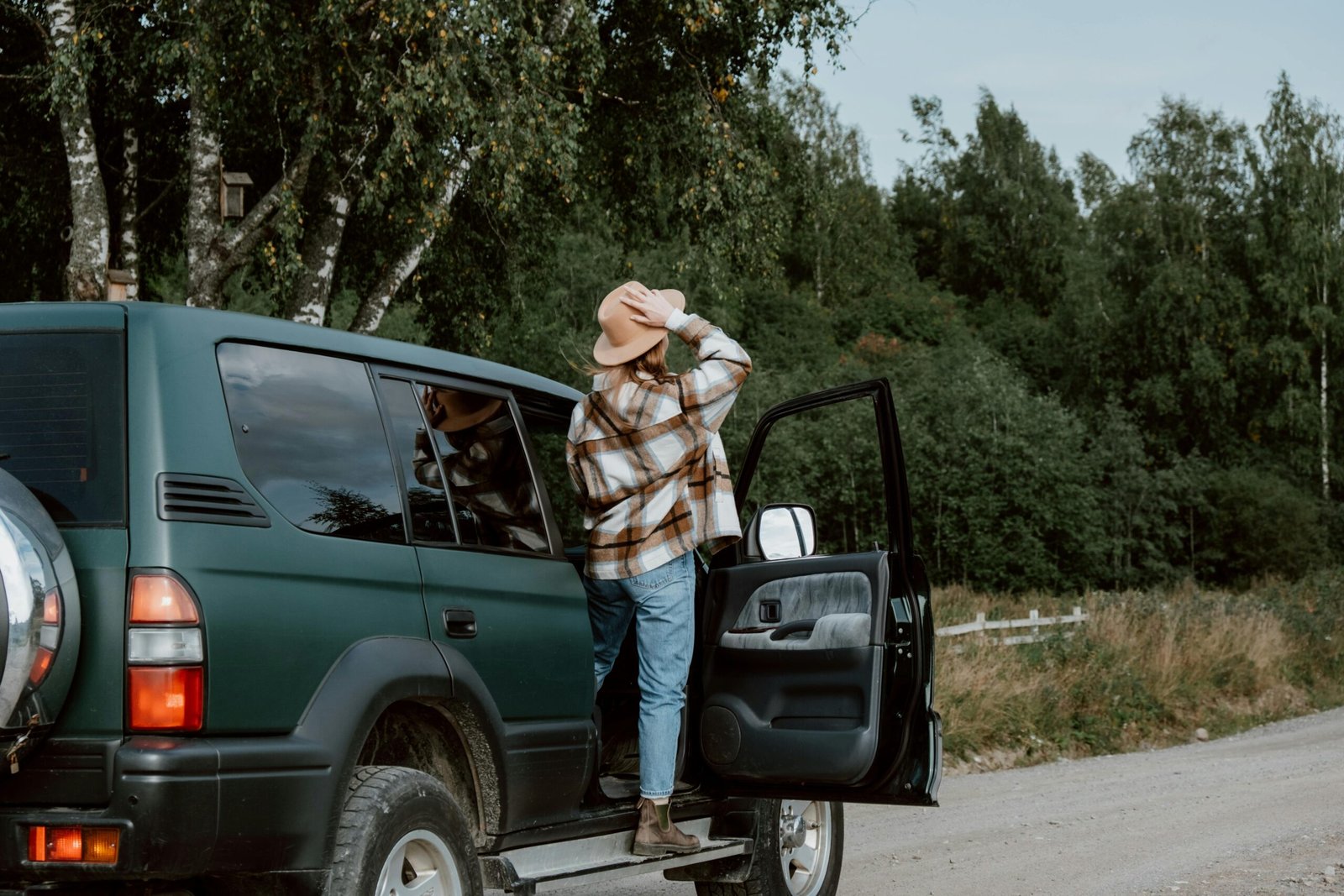 Person in plaid shirt standing by green SUV during a scenic road trip through nature.